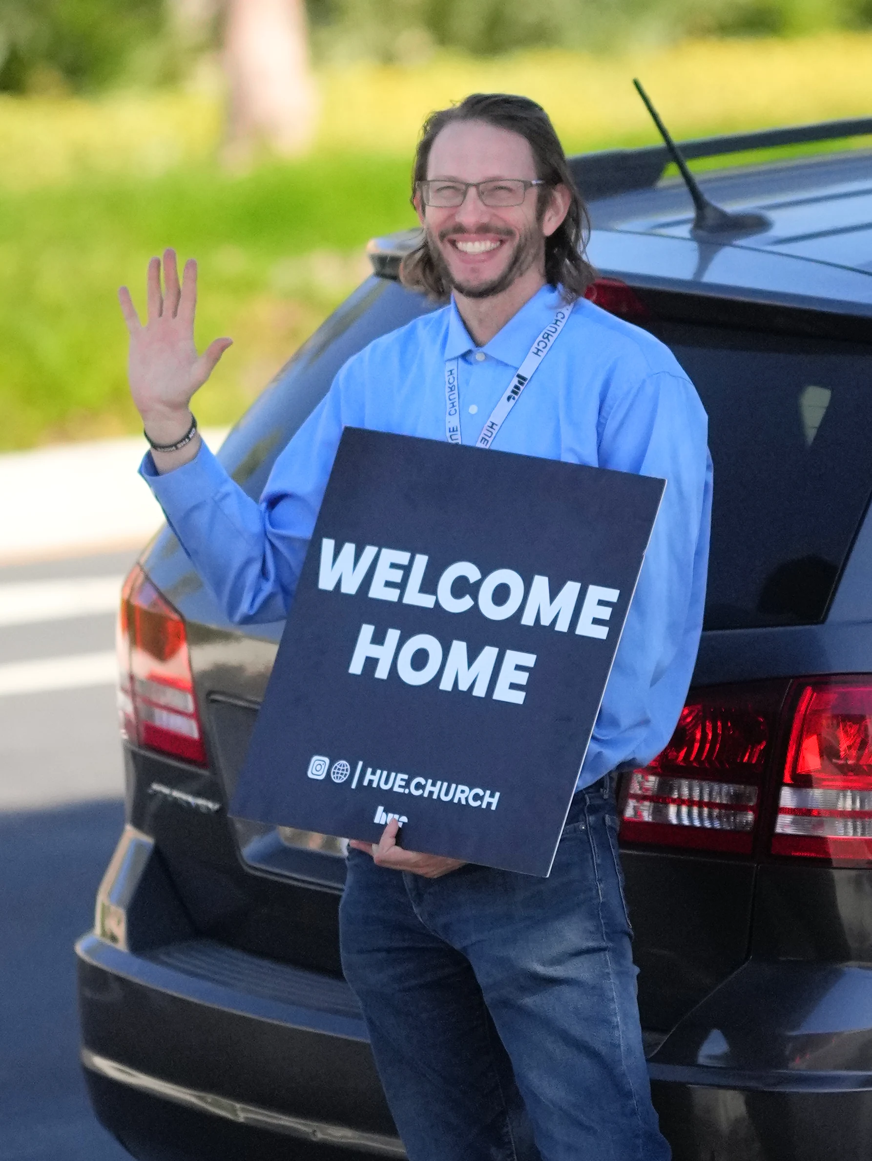 A smiling Hue volunteer waving with a Welcome Home sign on October 11